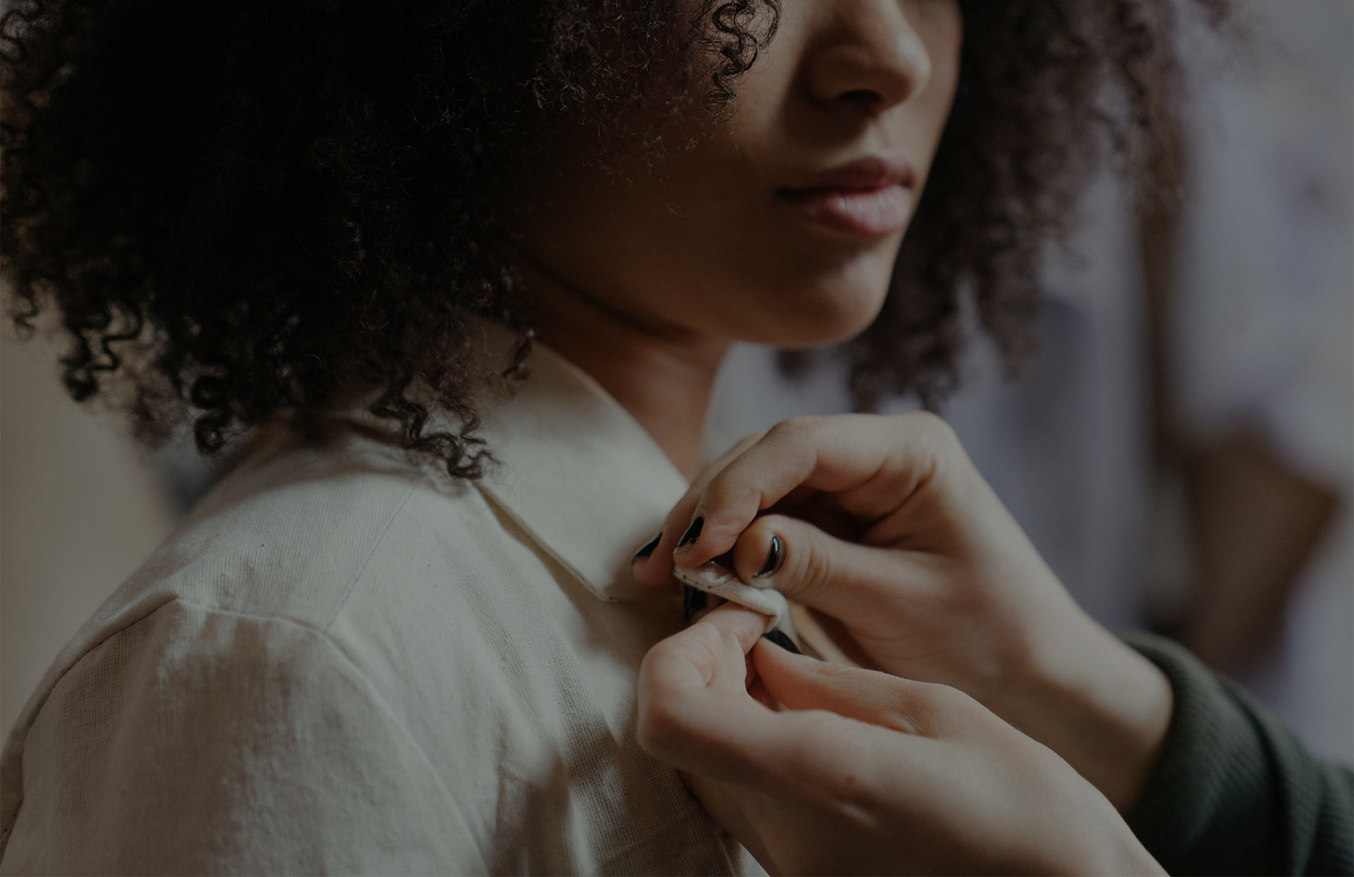 Tailor adjusting the collar of a woman’s shirt during a fitting.