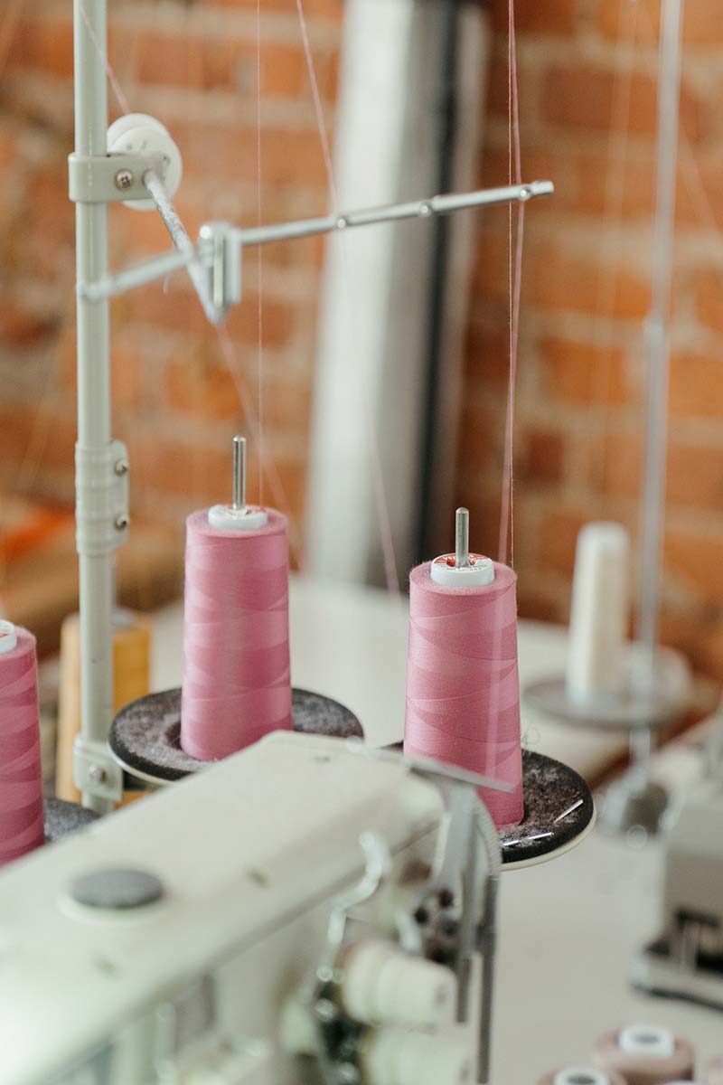 Close-up view of pink thread spools on an industrial sewing machine in a tailoring workshop with a brick wall in the background