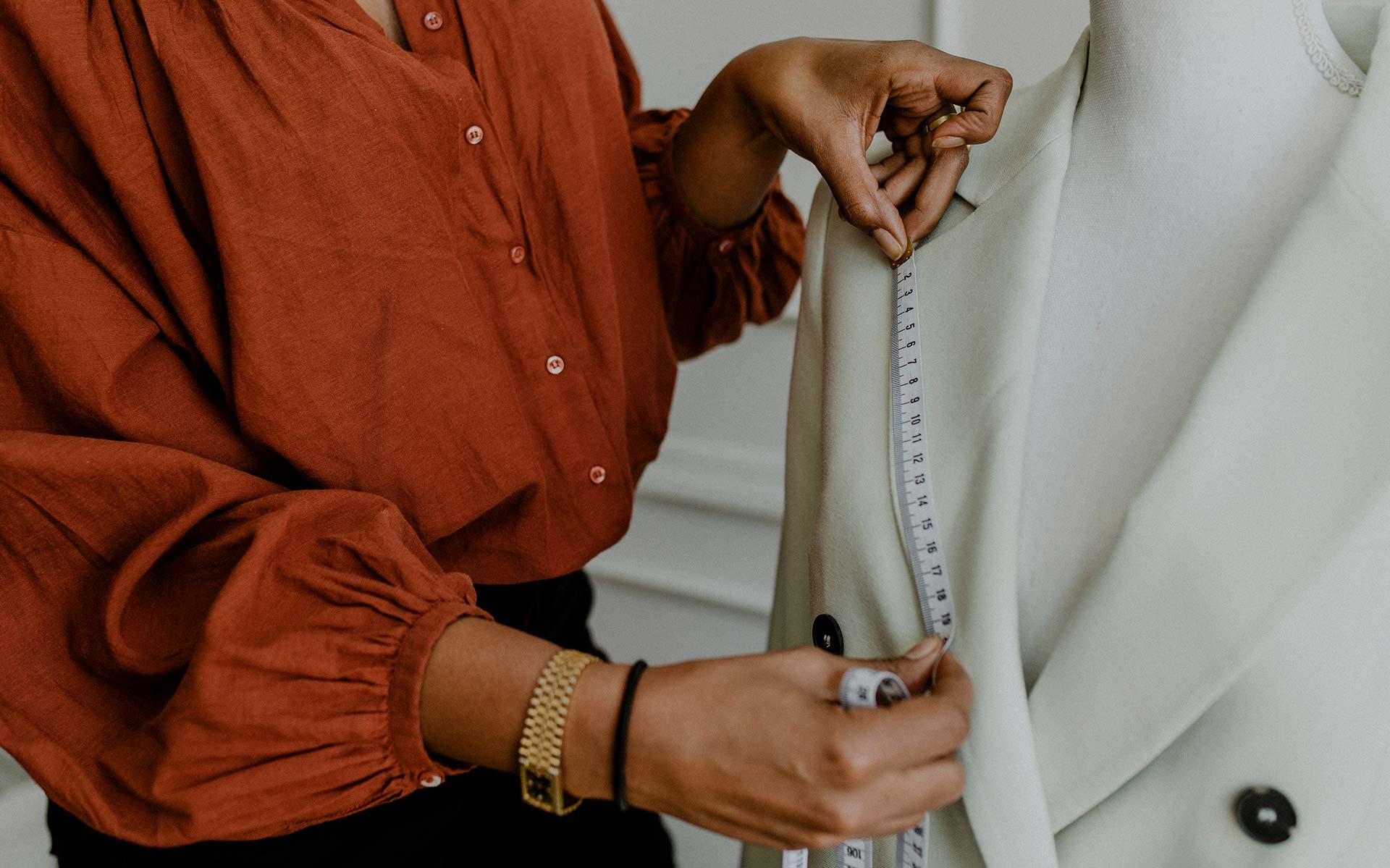 Tailor measuring the lapel of a cream-coloured coat on a mannequin using a measuring tape